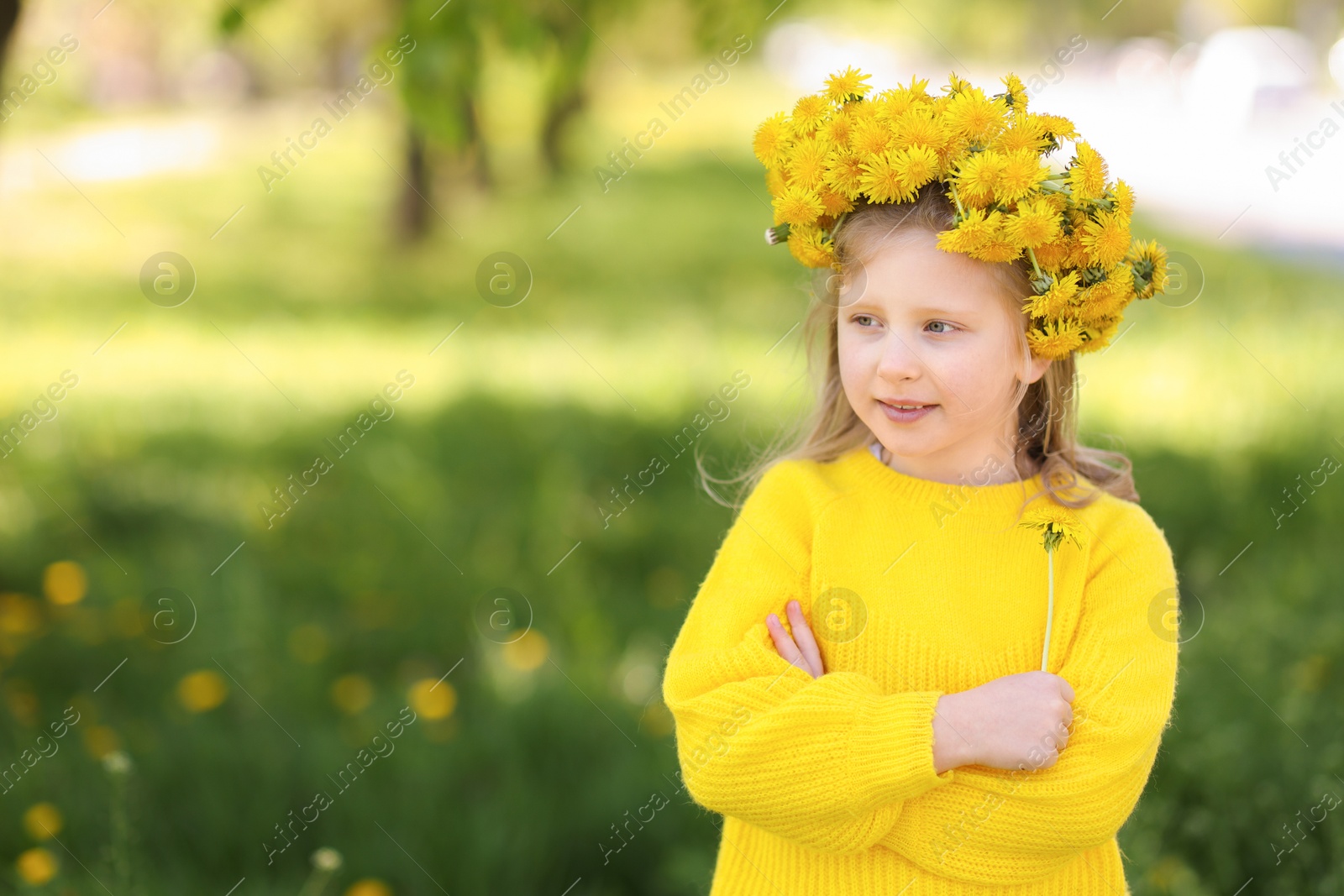 Cute little girl with beautiful flower wearing wreath of dandelions in park, space for text Photo of Cute little girl with beautiful flower wearing wreath of dandelions in park, space for text