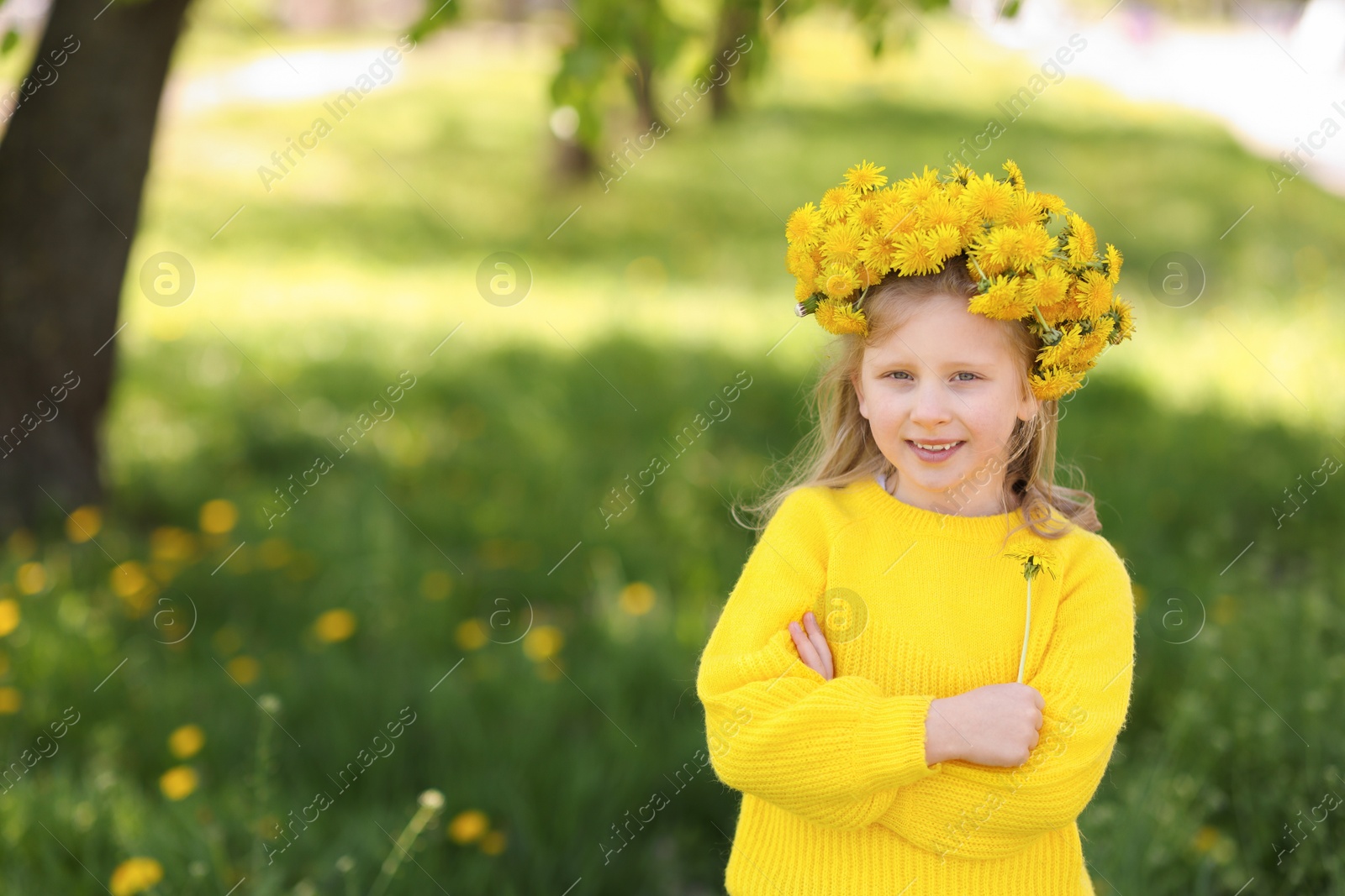Cute little girl with beautiful flower wearing wreath of dandelions in park, space for text Photo of Cute little girl with beautiful flower wearing wreath of dandelions in park, space for text