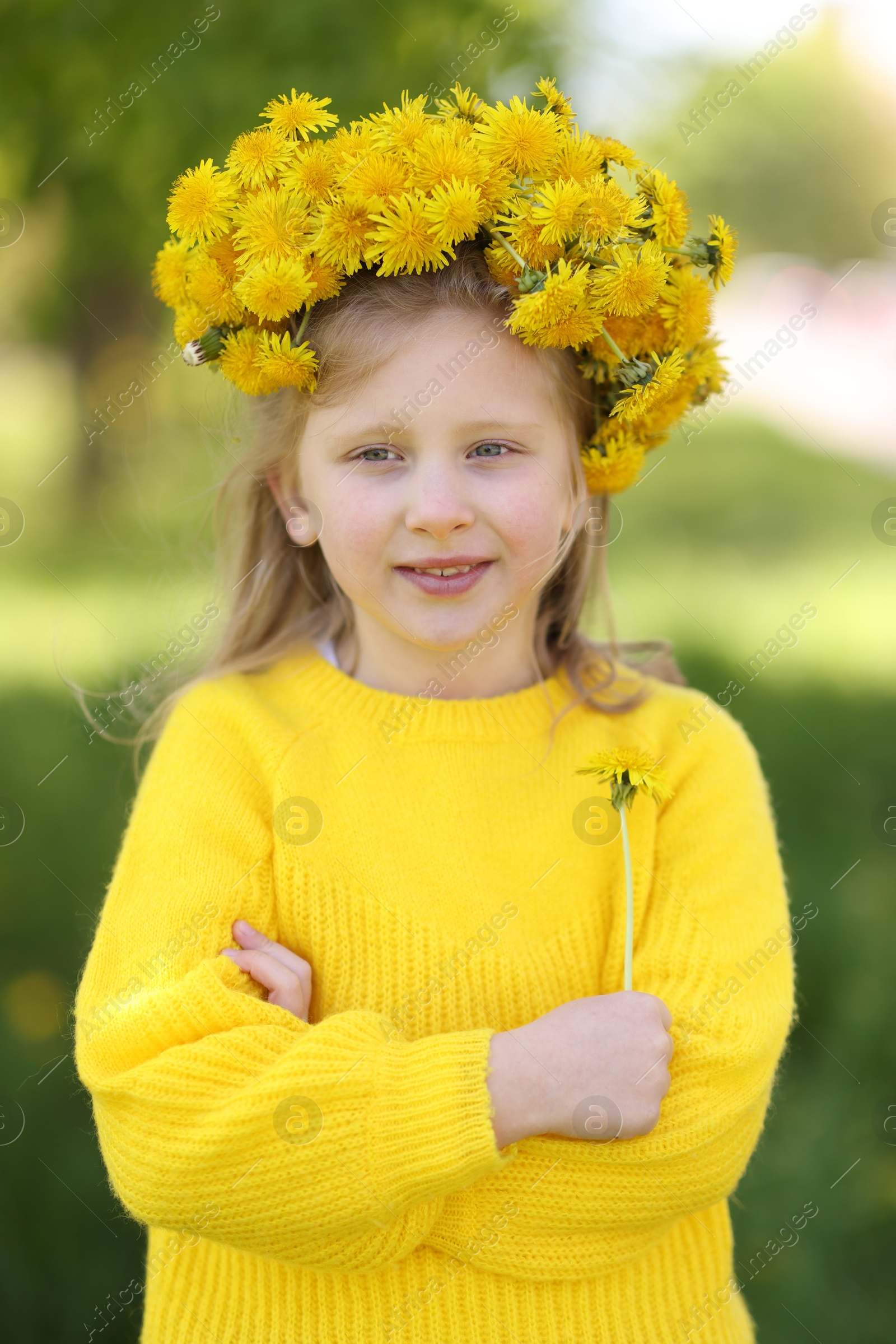 Cute little girl with beautiful flower wearing wreath of dandelions in park Photo of Cute little girl with beautiful flower wearing wreath of dandelions in park