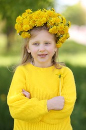 Photo of Cute little girl with beautiful flower wearing wreath of dandelions in park