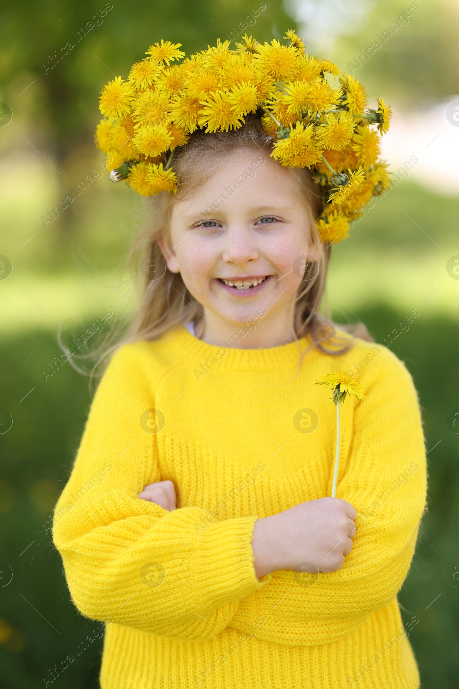 Cute little girl with beautiful flower wearing wreath of dandelions in park Photo of Cute little girl with beautiful flower wearing wreath of dandelions in park