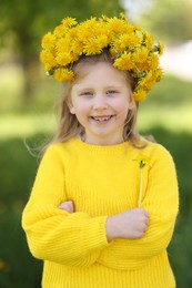 Photo of Cute little girl with beautiful flower wearing wreath of dandelions in park