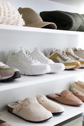 Photo of Different footwear and clothes on shelves indoors, closeup. Shoe storage