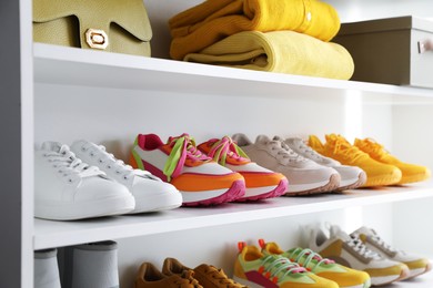 Photo of Different footwear, clothes and bag on shelves indoors, closeup. Shoe storage
