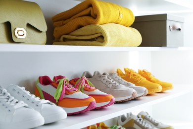 Photo of Different footwear, clothes and bag on shelves indoors, closeup. Shoe storage