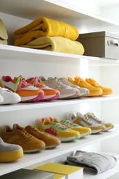 Photo of Different footwear and clothes on shelves indoors, closeup. Shoe storage