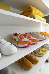 Photo of Different footwear and clothes on shelves indoors, closeup. Shoe storage