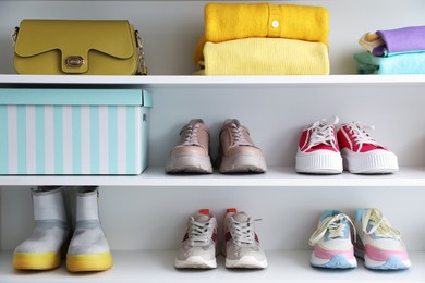 Photo of Different footwear, clothes and bag on shelves indoors. Shoe storage