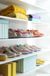 Photo of Different footwear and clothes on shelves indoors, closeup. Shoe storage