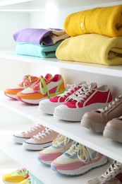 Photo of Different footwear and clothes on shelves indoors, closeup. Shoe storage