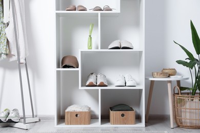 Photo of Shelving unit with different footwear, accessories, clothes and houseplant indoors. Shoe storage
