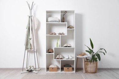 Photo of Shelving unit with different footwear, accessories, clothes and houseplant indoors. Shoe storage