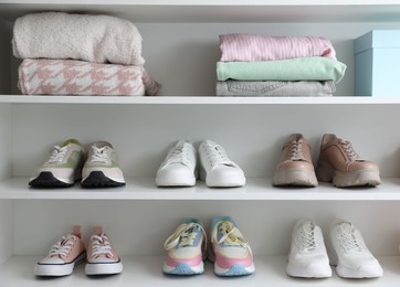 Photo of Different footwear and clothes on shelves indoors. Shoe storage
