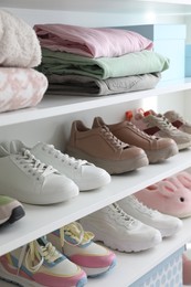 Photo of Different footwear and clothes on shelves indoors, closeup. Shoe storage