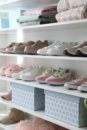 Photo of Different footwear and clothes on shelves indoors, closeup. Shoe storage
