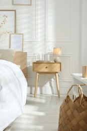 Photo of Bedside table with lamp, jug of water and glass near bed in room. Interior design
