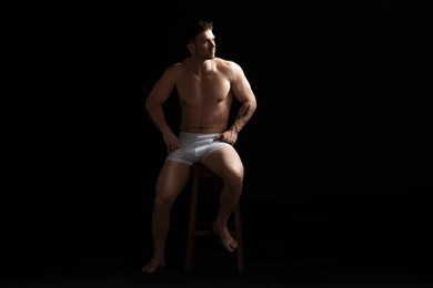 Photo of Young man in stylish white underwear on chair against black background