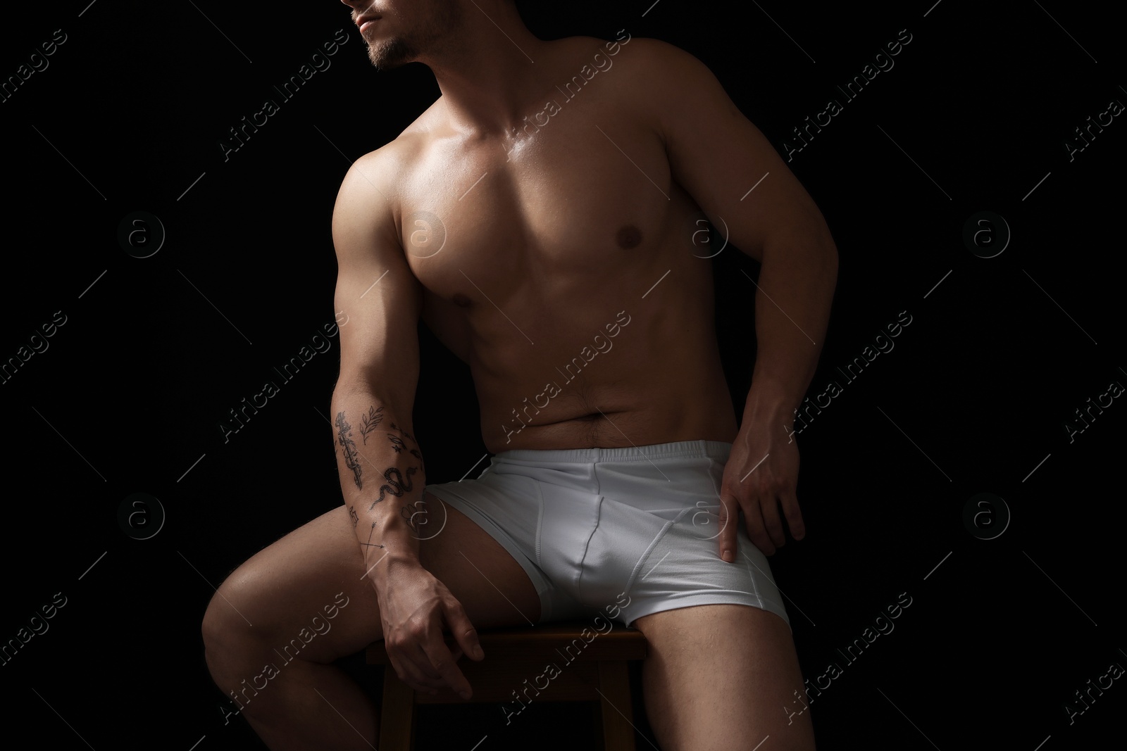 Young man in stylish white underwear on chair against black background, closeup Photo of Young man in stylish white underwear on chair against black background, closeup