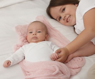 Photo of Cute girl and her little sister on bed at home