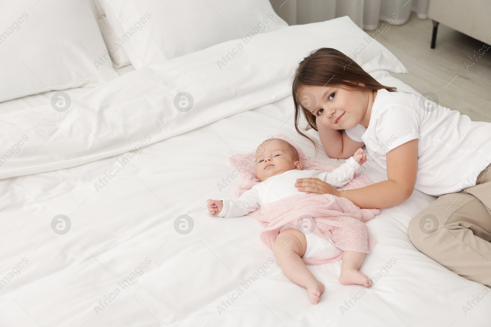 Cute girl and her little sister on bed at home, space for text Photo of Cute girl and her little sister on bed at home, space for text