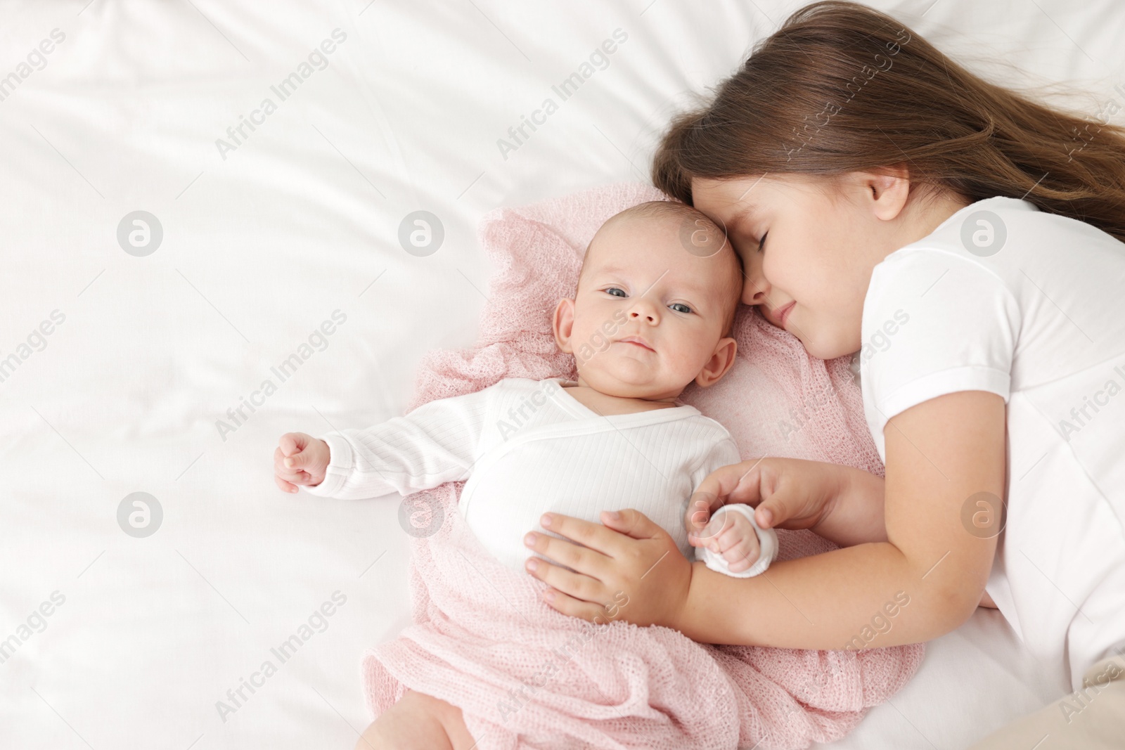 Cute girl and her little sister on bed at home, space for text Photo of Cute girl and her little sister on bed at home, space for text
