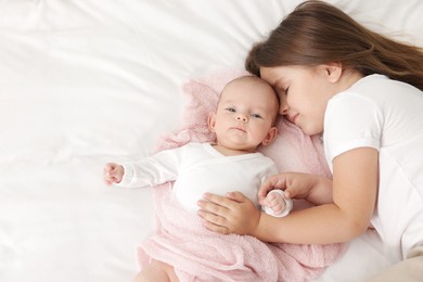 Photo of Cute girl and her little sister on bed at home, space for text