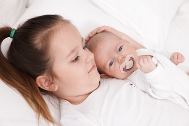Photo of Cute girl and her little sister on bed at home