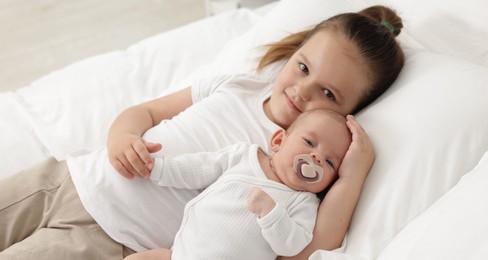 Photo of Cute girl and her little sister on bed at home
