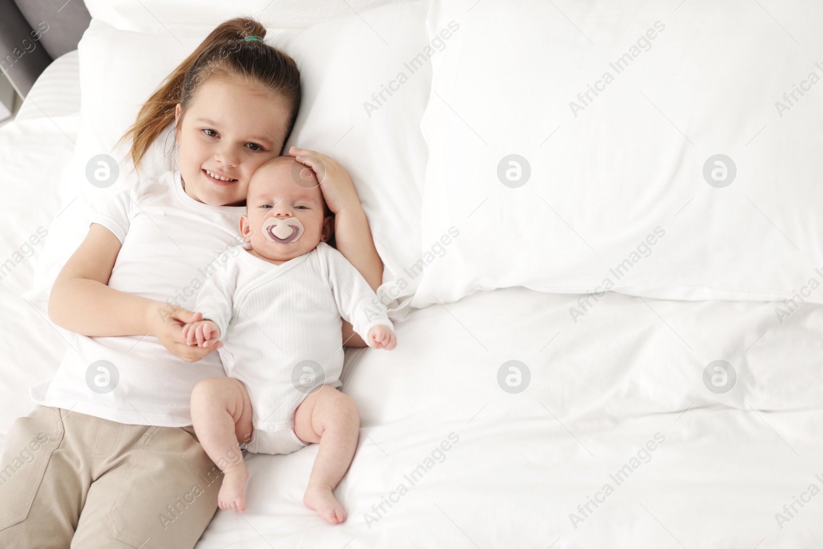 Cute girl and her little sister on bed at home, space for text Photo of Cute girl and her little sister on bed at home, space for text