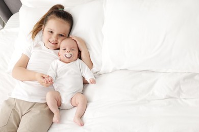 Photo of Cute girl and her little sister on bed at home, space for text