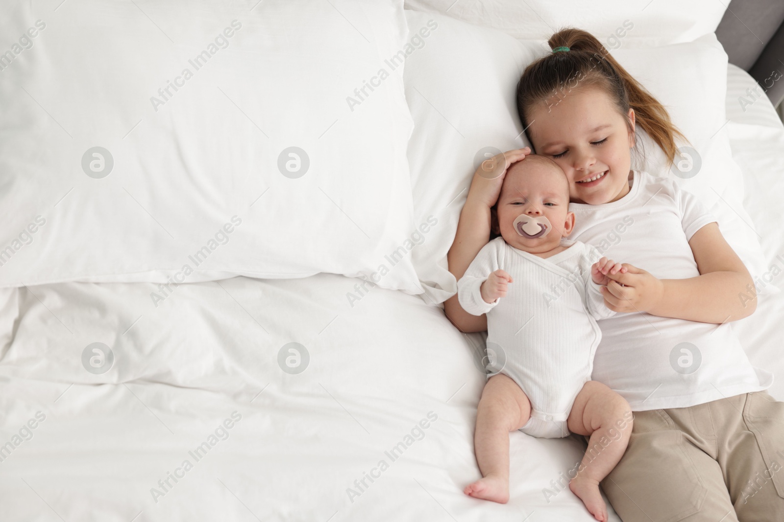 Cute girl and her little sister on bed at home, space for text Photo of Cute girl and her little sister on bed at home, space for text