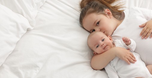 Photo of Cute girl and her little sister on bed at home, above view. Space for text