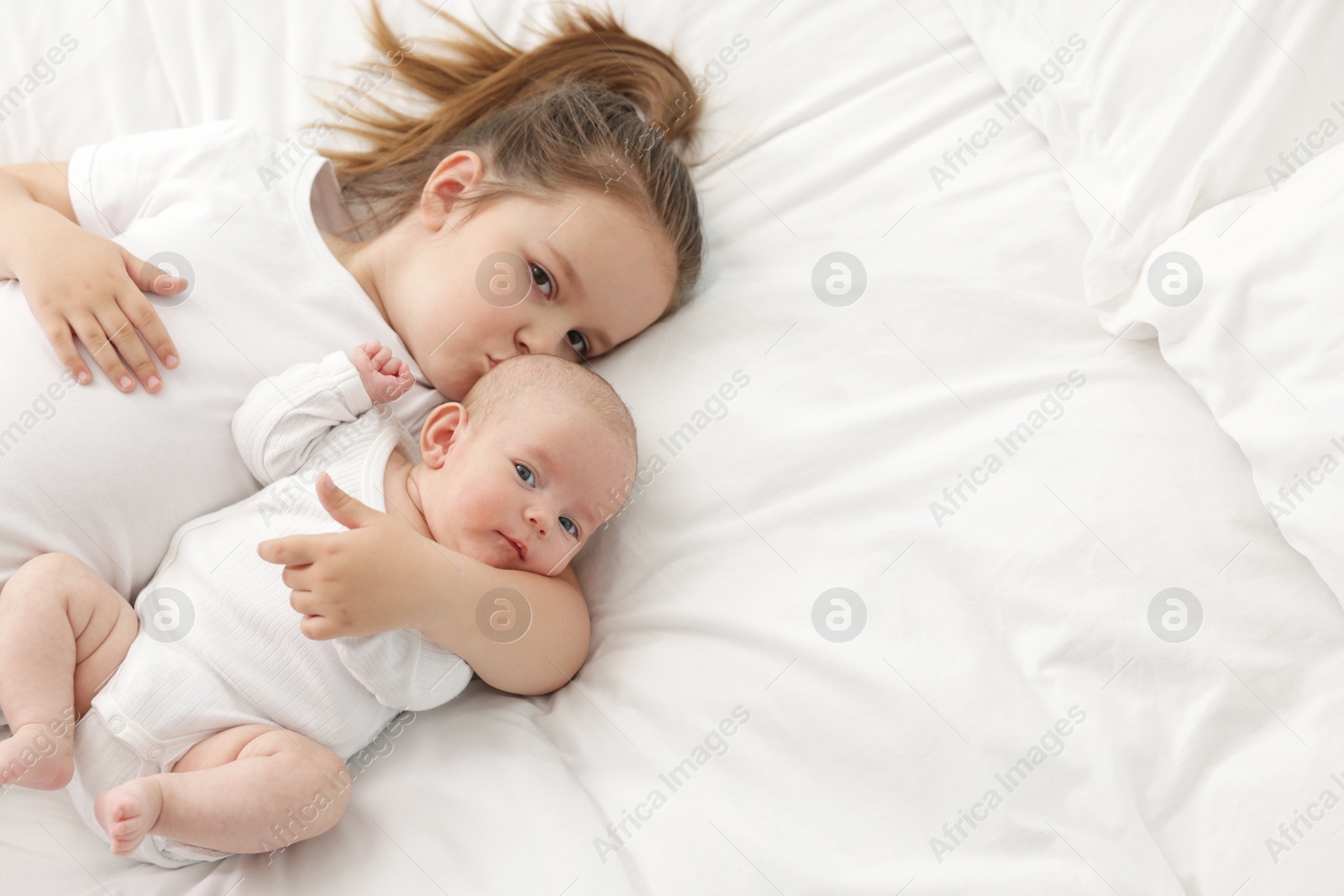 Cute girl and her little sister on bed at home, above view. Space for text Photo of Cute girl and her little sister on bed at home, above view. Space for text