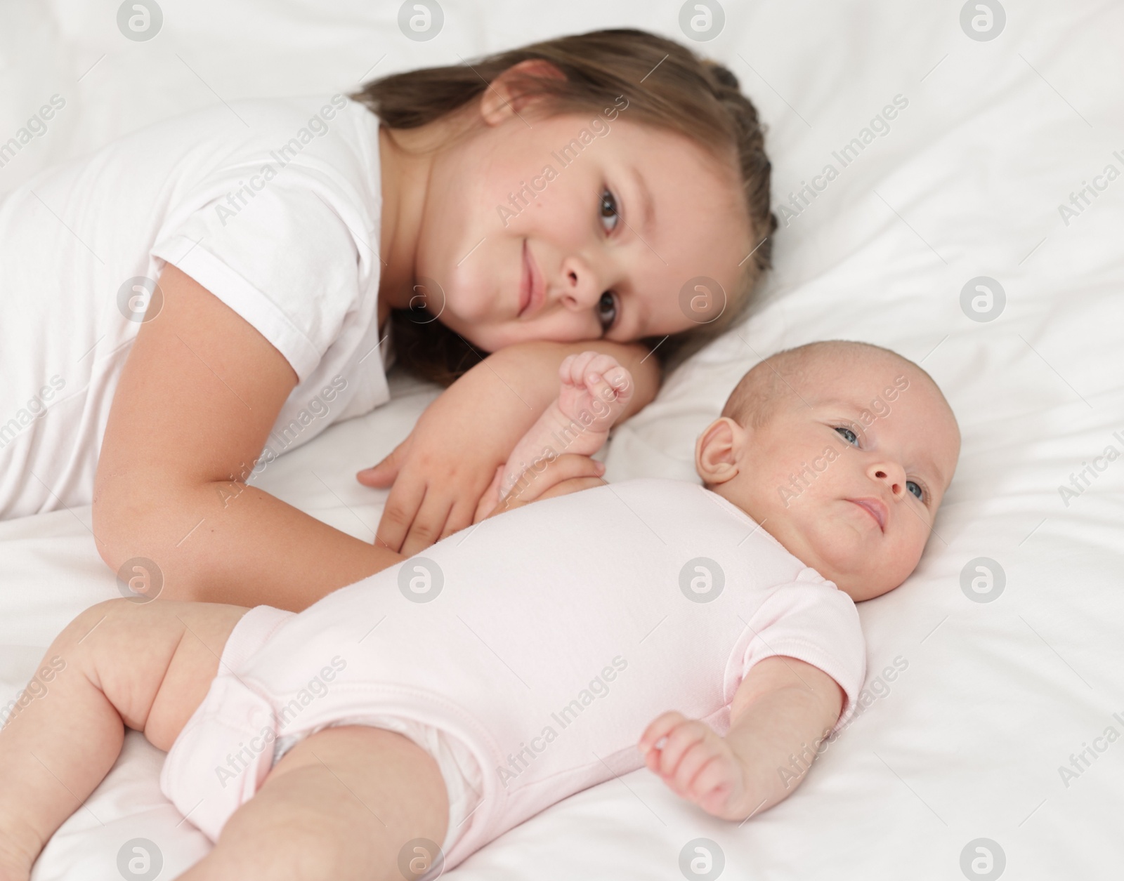 Cute girl and her little sister on bed at home Photo of Cute girl and her little sister on bed at home