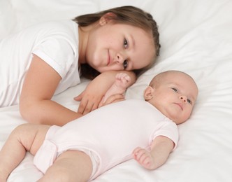 Photo of Cute girl and her little sister on bed at home