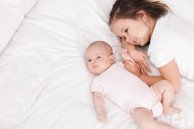 Photo of Cute girl and her little sister on bed at home, above view. Space for text