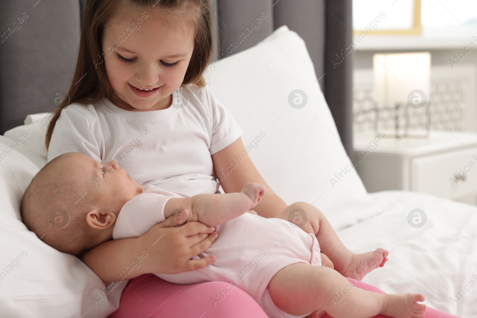Cute girl and her little sister on bed at home, space for text Photo of Cute girl and her little sister on bed at home, space for text