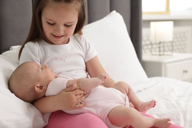 Photo of Cute girl and her little sister on bed at home, space for text