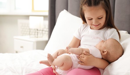 Photo of Cute girl and her little sister on bed at home, space for text