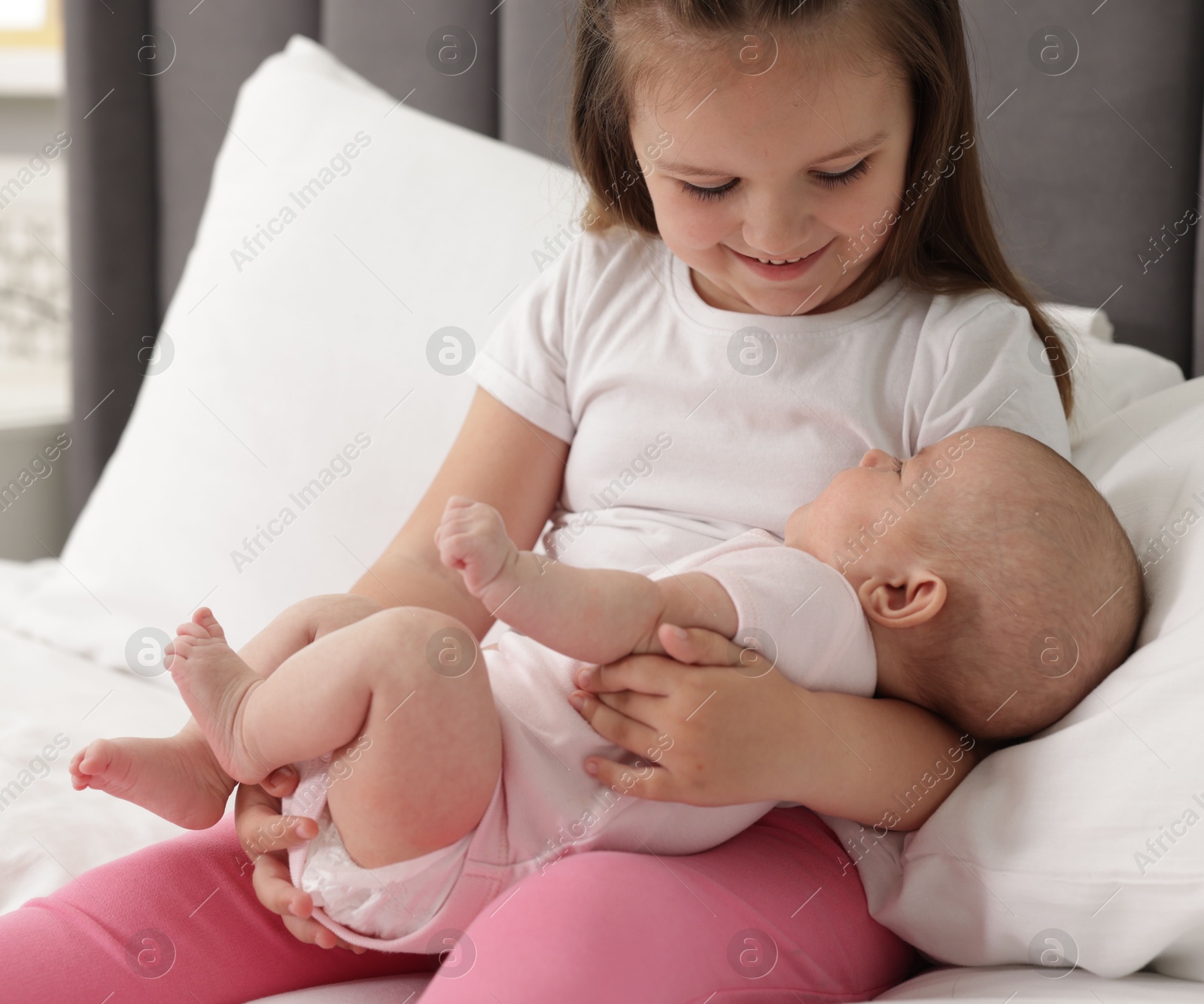 Cute girl and her little sister on bed at home Photo of Cute girl and her little sister on bed at home