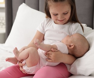 Photo of Cute girl and her little sister on bed at home