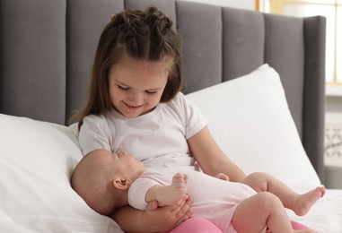 Photo of Cute girl and her little sister on bed at home