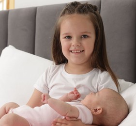 Photo of Cute girl and her little sister on bed at home