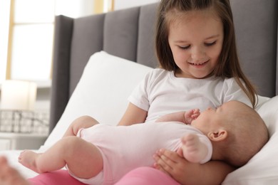 Photo of Cute girl and her little sister on bed at home