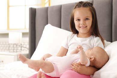 Photo of Cute girl and her little sister on bed at home