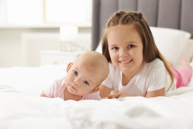 Photo of Cute girl and her little sister on bed at home