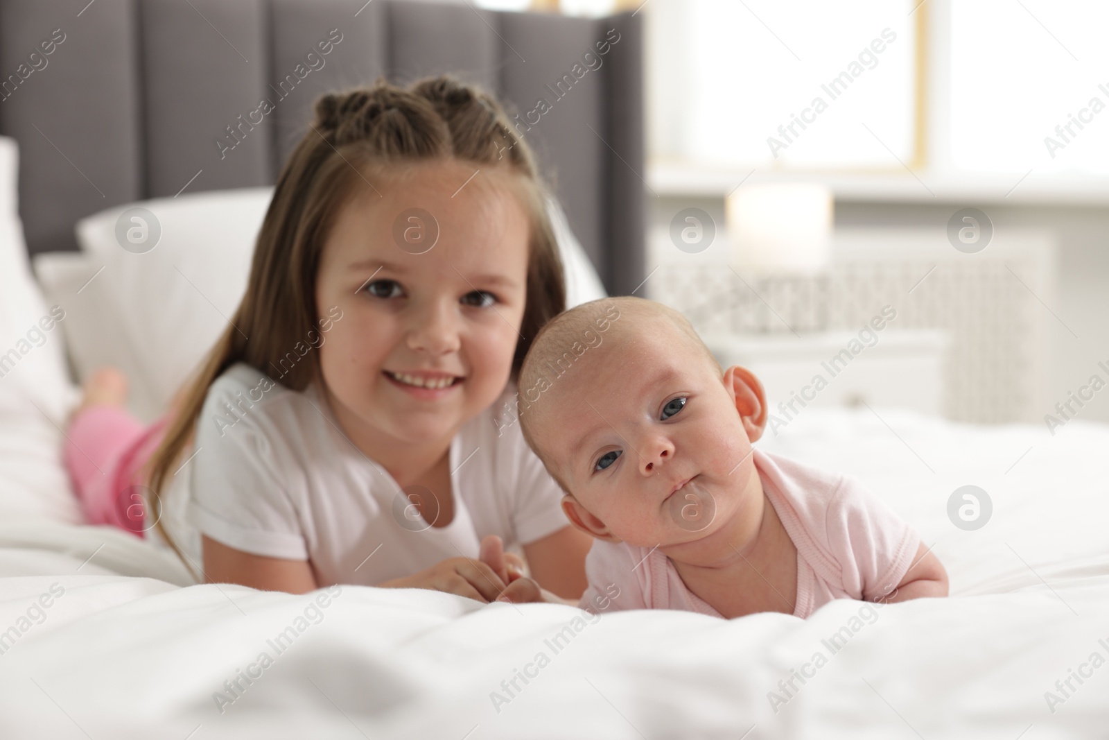 Cute girl and her little sister on bed at home Photo of Cute girl and her little sister on bed at home