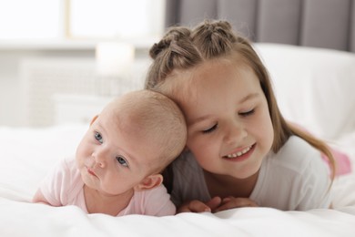 Photo of Cute girl and her little sister on bed at home