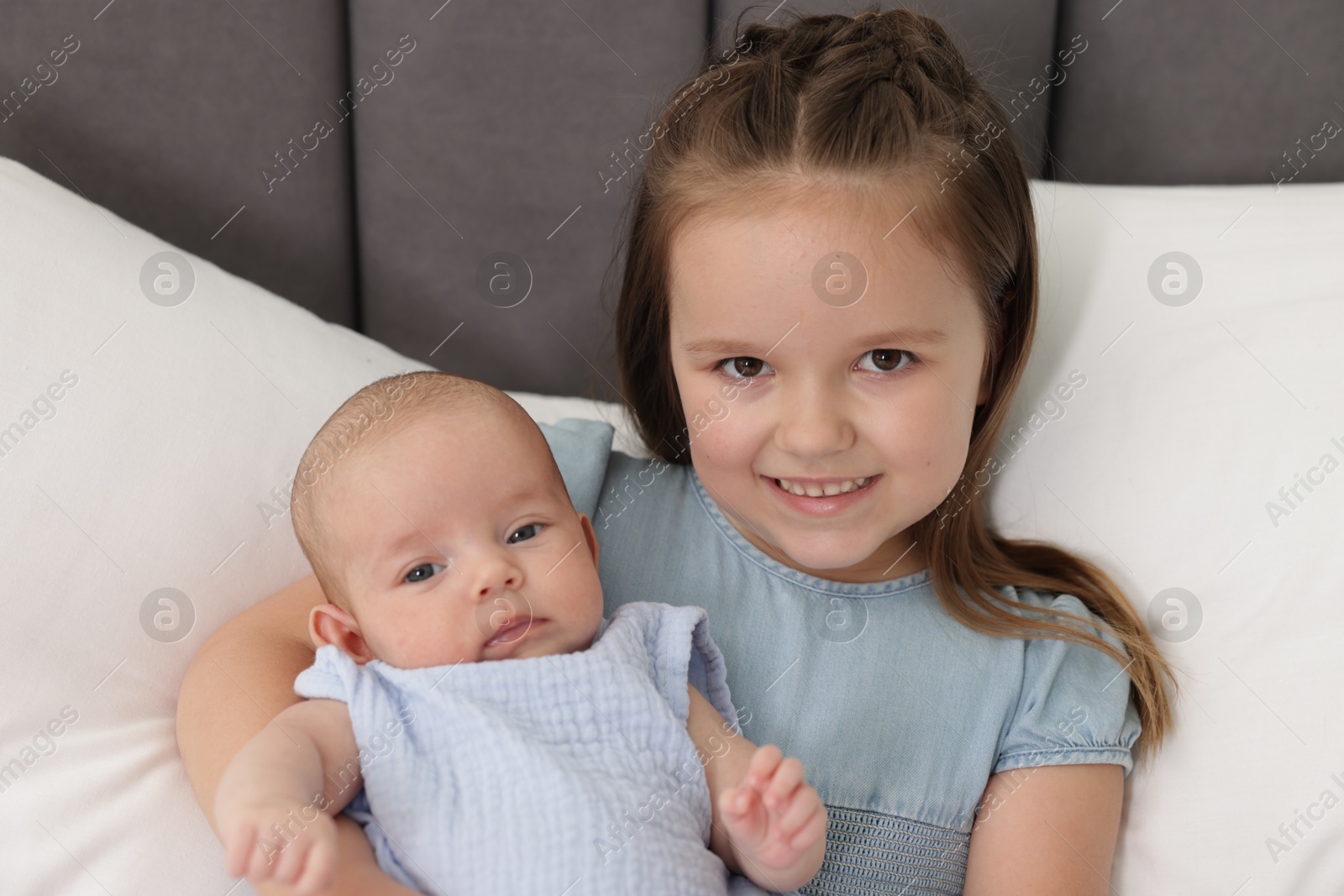 Cute girl and her little sister on bed at home Photo of Cute girl and her little sister on bed at home