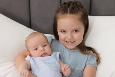 Photo of Cute girl and her little sister on bed at home